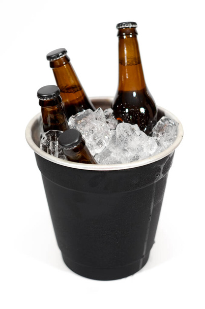 Ein schwarzer Eimer mit vier braunen Glasflaschen Bier auf weißem Hintergrund. - Foto, Bild
