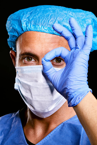 pozytywny portret przystojnego lekarza kaukaskiego człowieka noszącego niebieską papierową maskę ochronną wirusa na czarnym, izolowanym tle - Zdjęcie, obraz