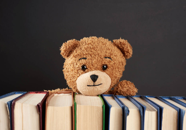 αρκουδάκι κρυφοκοιτάζει πίσω από μια στοίβα βιβλία, μαύρο φόντο, πίσω στο σχολείο - Φωτογραφία, εικόνα