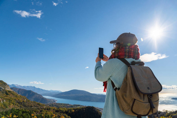 Traveler with a backpack and a smartphone stands on a mountain  - Фото, изображение
