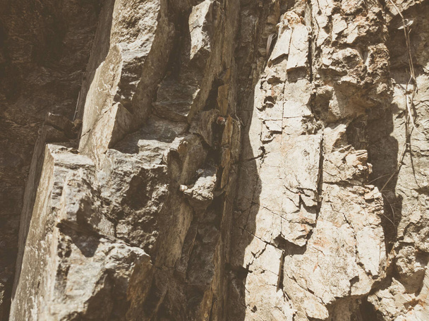 Natural background. Closeup edged shabby cliff cracks. Gray-brown stone rock texture of mountains. Vintage and faded matt style colour in tinted photo. Concept of geolog, mountaineering or hard work - Fotografie, Obrázek
