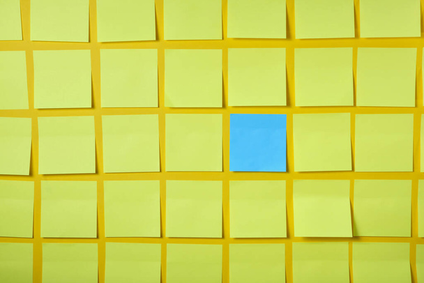 one blue and many light yellow sticky notes on yellow background, brainstorming concept - Zdjęcie, obraz