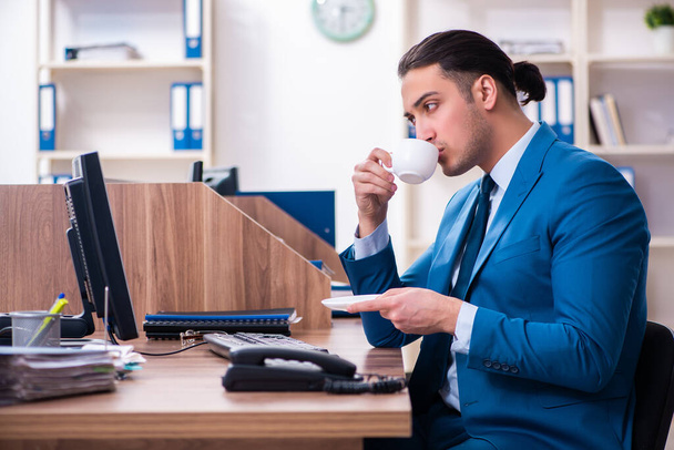 Νέος όμορφος επιχειρηματίας κάθεται στο γραφείο - Φωτογραφία, εικόνα