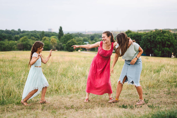 Three sister girls playing on the park outdoor. 3 girls, sisters, girlfriends in the field. Happy mother with younger and older daughter, two children plays in the meadow in summer in dresses. - Photo, Image