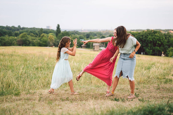 Drei erwachsene kaukasische Schwestern spielen und haben Spaß auf dem Feld. Eine Familie aus drei jungen Frauen lacht und verbringt den Sommer in der Natur. Glückliches Kind, Mutter und Schwester rennen und spielen im Freien. - Foto, Bild