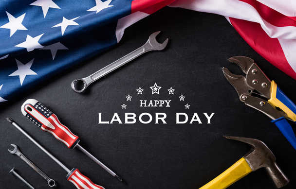 Happy Labor day concept. American flag with different construction tools on black table background, with copy space for text. - Photo, Image