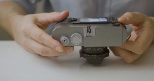 Der Kaukasier beobachtet die alte Kamera auf einem weißen Tisch  - Filmmaterial, Video