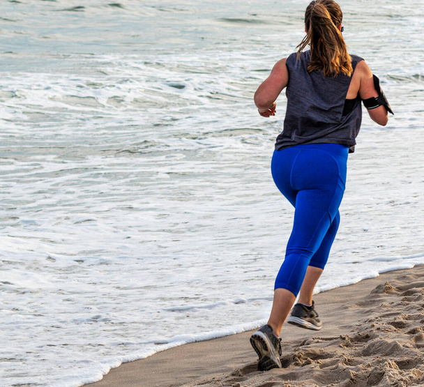 A female in blue spandex is running at the beach close to the ocean on Fire Island. - Φωτογραφία, εικόνα