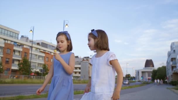 dwie słodkie dziewczynki spacerują po mieście i jedzą lody - Materiał filmowy, wideo