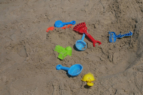 Algunos juguetes de playa están hechos de plástico dispersos aleatoriamente en la arena de la playa. Abandonado por los niños. - Foto, imagen