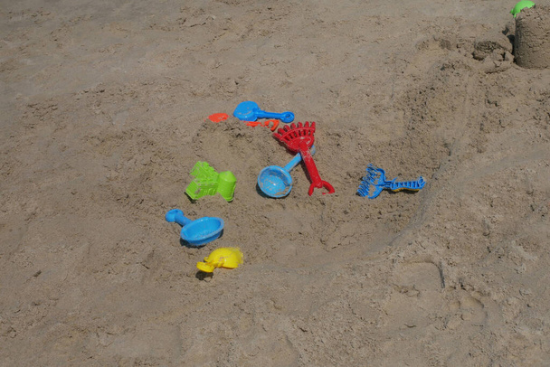 Niektóre zabawki plażowe są wykonane z plastiku rozrzuconego losowo na piasku plażowym. Porzucony przez dzieci. - Zdjęcie, obraz
