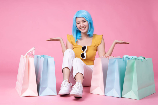 Portrait of a pretty excited asian girl with colorful shopping bags showing  isolated over pink background .Asian shopaholic woman carrying shopping bags in colorful for summer sale concept .young blue hair girl . - 写真・画像