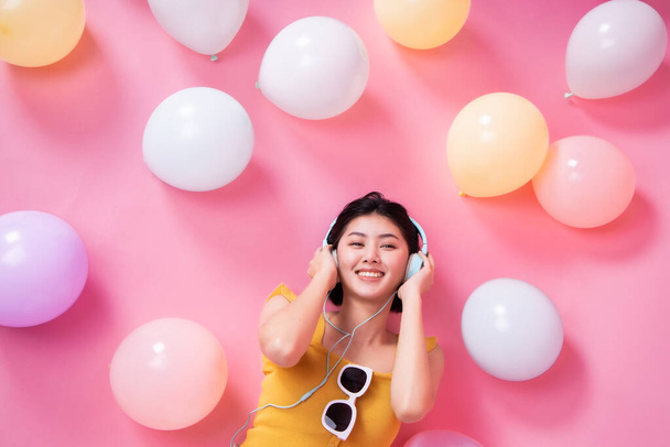 Asian Beauty girl with colorful air balloons laughing over pink background. Young woman on birthday holiday party. Celebrating with pastel color balloon.She listen music and dance. - Photo, Image