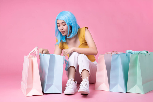 Portrait of a pretty excited asian girl with colorful shopping bags showing  isolated over pink background .Asian shopaholic woman carrying shopping bags in colorful for summer sale concept .young blue hair girl . - Fotó, kép