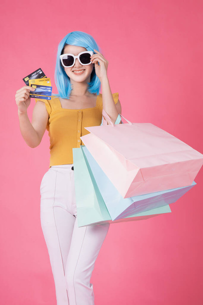 Portrait of a pretty excited asian girl with colorful shopping bags showing  isolated over pink background .Asian shopaholic woman carrying shopping bags in colorful for summer sale concept .young blue hair girl . - Fotografie, Obrázek
