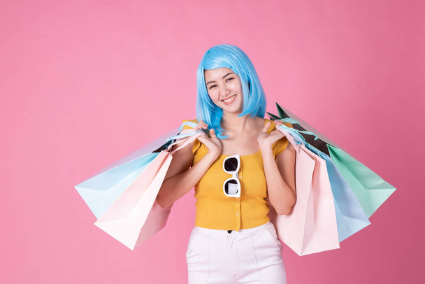 Portrait of a pretty excited asian girl with colorful shopping bags showing  isolated over pink background .Asian shopaholic woman carrying shopping bags in colorful for summer sale concept .young blue hair girl . - Фото, изображение