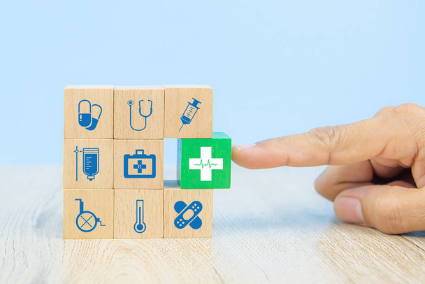 Χέρι επιλέξτε ιατρικό εικονίδιο σε κύβο ξύλινα μπλοκ παιχνιδιών στοίβα με άλλα ιατρικά σύμβολα έννοιες της θεραπείας ασθενειών και την ασφάλεια υγείας. - Φωτογραφία, εικόνα