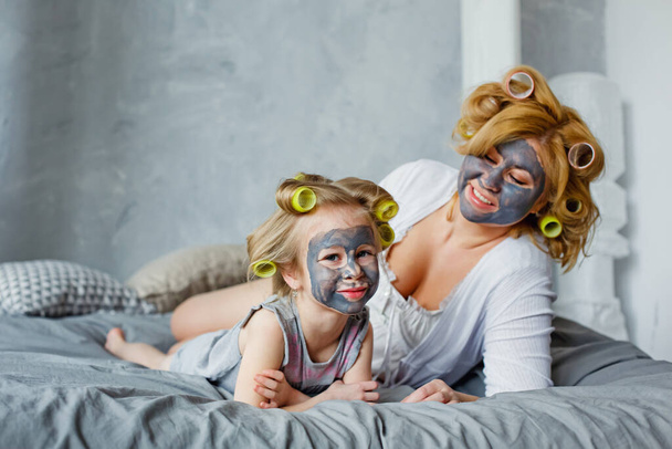 Мать и ребенок делают косметические процедуры вместе. Счастливая мама с маленькой дочкой делают маску для лица в спальне. Концепция салона красоты, Wellness Spa. - Фото, изображение