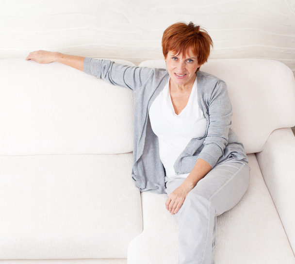 Happy mature woman on sofa - Фото, изображение