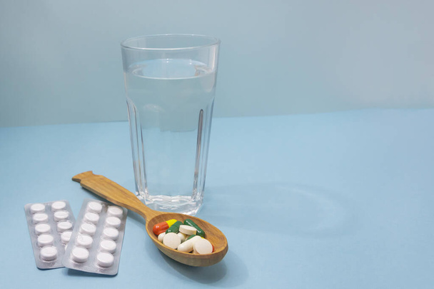 Lot of pills in spoon and glass of water on blue background. Medical concept. Excessive drug use. Copy space, selective focus. - Foto, afbeelding