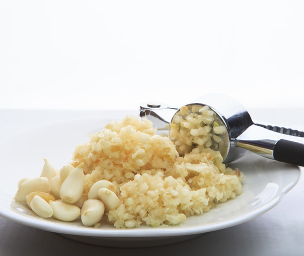 Aglio fresco schiacciato da frantoio di aglio su piatto bianco su cucina
 - Foto, immagini