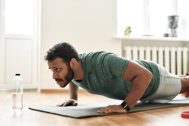 Fight for fit body. Young active man looking focused, exercising, doing push ups during morning workout at home. Sport, healthy lifestyle - Foto, afbeelding
