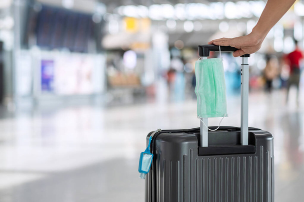 国際空港ターミナル、保護コロナウイルス病(Covid-19)感染症で外科用フェイスマスクとアルコールゲルハンド消毒剤付き荷物バッグ。新しいノーマルと旅行バブルの概念 - 写真・画像