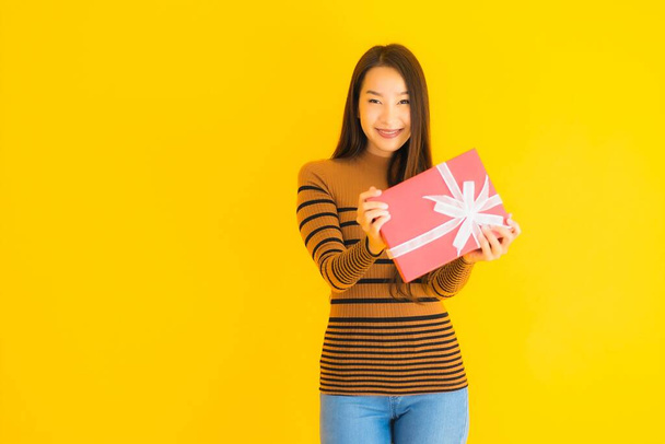 Portrait beautiful young asian woman happy smile with red gift box on yellow isolated background - Foto, immagini