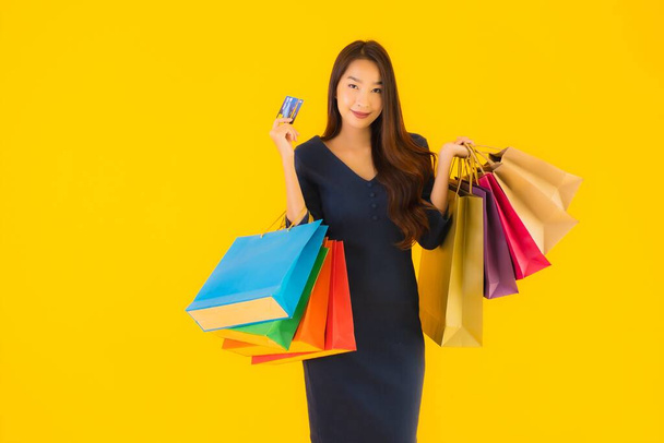 Портрет красива молода азіатська жінка з сумкою кредитною карткою та смартфоном жовтий ізольований фон
 - Фото, зображення