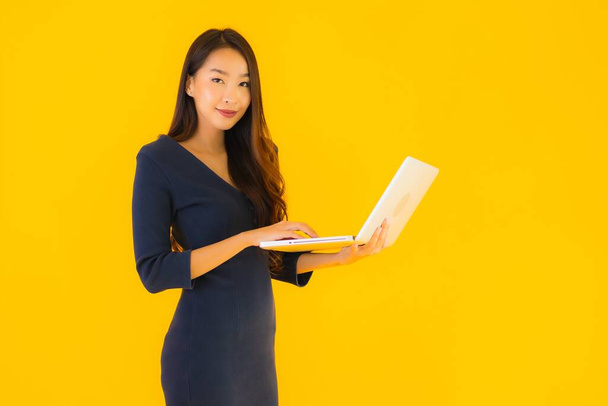 Portrait beautiful young asian woman with laptop or computer on yellow isolated background - Φωτογραφία, εικόνα