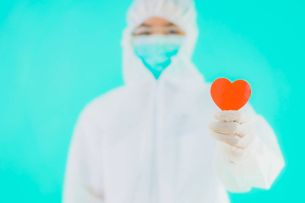 Retrato hermosa joven asiática médico mujer usar ppe o equipo de protección personal para proteger de coronavirus o covid19 mostrar el corazón en azul aislado fondo
 - Foto, imagen