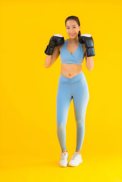 Muotokuva kaunis nuori aasialainen nainen käyttää urheiluvaatteita nyrkkeilyllä keltaisella eristetyllä taustalla - Valokuva, kuva