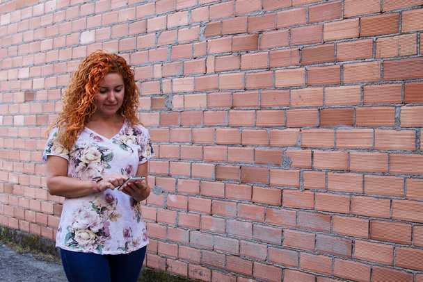 woman using mobile phone with brick wall background - Photo, Image