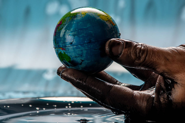 Die Hand des schmutzigen Mannes zog die Erde in Form einer Erdkugel aus dem Öl und hält sie vorsichtig. Konzept eines umweltfreundlichen Verhaltens, das natürliche Ressourcen nutzt und der Umwelt schadet - Foto, Bild