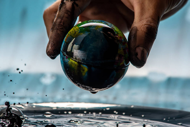 La main de l'homme souillé tire la Terre sous la forme d'un globe hors du pétrole. Concept de sauver la planète, d'utiliser les ressources naturelles et de nuire à l'environnement - Photo, image