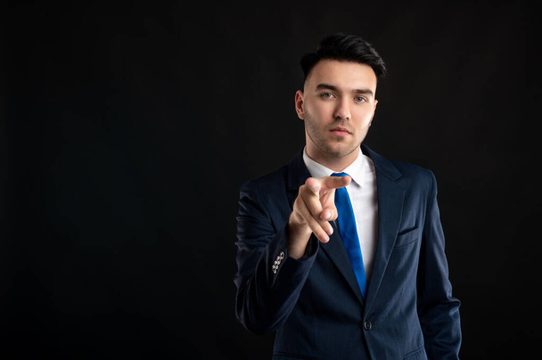 Portrait of business man wearing blue business suit and tie doing I am watching you gesture posing on isolated black background with copy space advertising area - 写真・画像