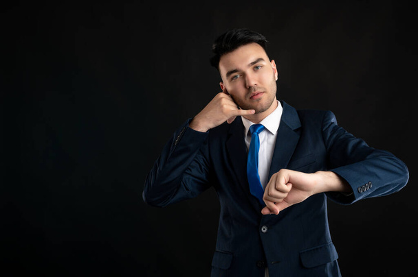 Portrait of business man wearing blue business suit and tie showing it's time gesture isolated on black background with copy space advertising area - Foto, Bild