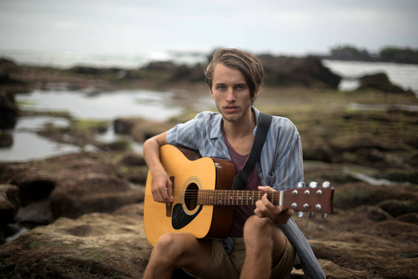 Romantische jongeman met een gitaar op het strand - Foto, afbeelding