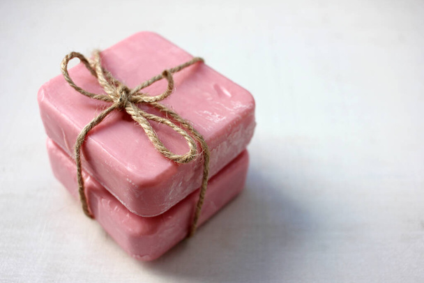 Két darab rózsaszín, kézzel készített szappan zsineggel a fehér fából készült háttéren. Szelektív fókusz, másolás - Fotó, kép