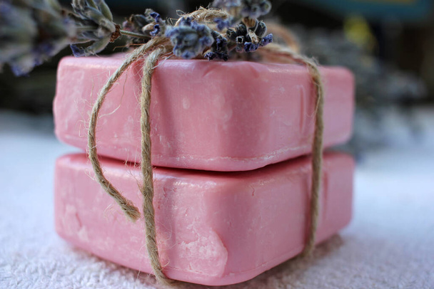Dos barras de jabón rosa hecho a mano atadas con flores de cordel y lavanda sobre el fondo de madera blanca. Enfoque selectivo, espacio de copia - Foto, imagen