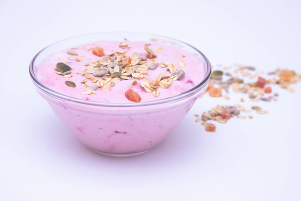 A bowl of berry yogurt with grains and fruit chunks on it on a white surface - Фото, изображение