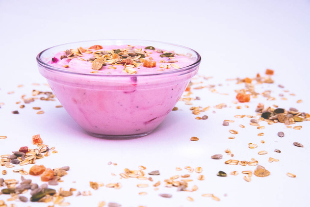 Чаша ягодного йогурта с зерном и фруктовыми ломтиками на белой поверхности - Фото, изображение