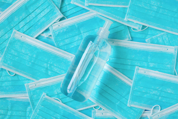 青い外科用フェイスマスクテクスチャの背景の保護COVID-19コロナウイルスに対するアルコールハンドサニタイザージェルボトル。医療・医療の概念 - 写真・画像