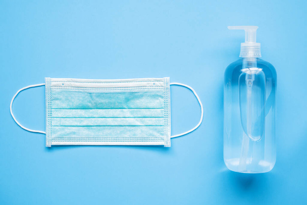 Alcol mano igienizzante bottiglia di gel con maschera chirurgica su sfondo blu protezione contro COVID-19 coronavirus. Concetto sanitario e medico - Foto, immagini