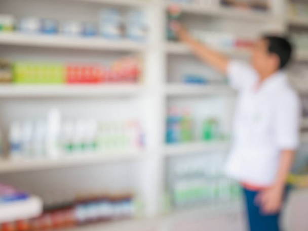 wazig beeld van apotheker die geneesmiddelen van de plank haalt in de apotheek - Foto, afbeelding