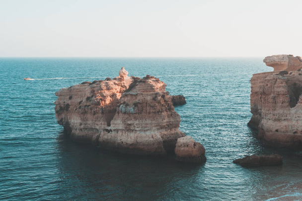 Sea stacks and rock cliffs at a shore under a bright sky - Фото, зображення