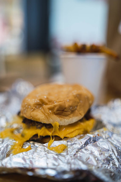 A vertical shot of cheesy burger and cup of fries on a table - 写真・画像