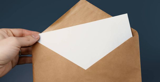 Cropped view of man holding craft envelope with blank white card on blue background - Fotografie, Obrázek