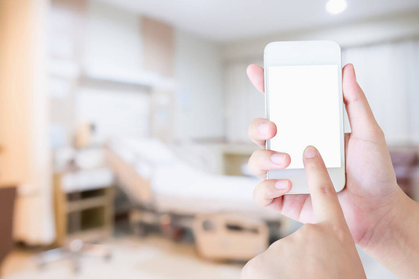 Mano femenina sosteniendo teléfono móvil inteligente con fondo hospital borroso - Foto, Imagen