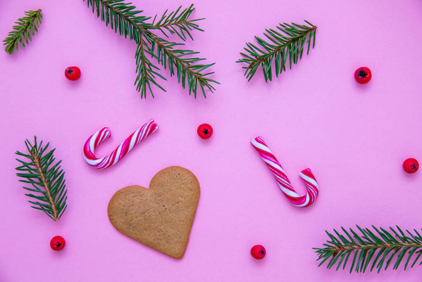 A flat lay shot of candy canes, fir branches, Christmas berries and a heart cookie on a pink surface - Foto, afbeelding